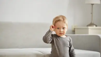Malé dítě ve šedém tričku stojí na pohovce.