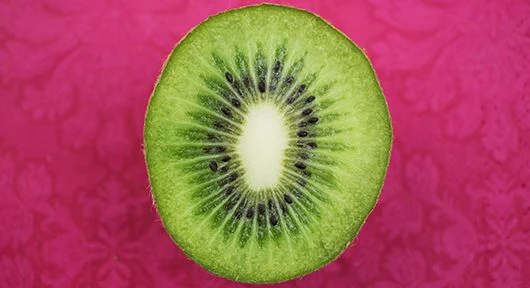 Průřez zeleného kiwi na růžovém pozadí.