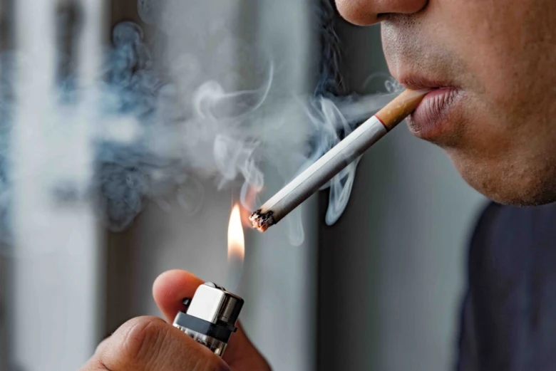 Muž zapaluje cigaretu zapaľovačem s výfukem kouře.