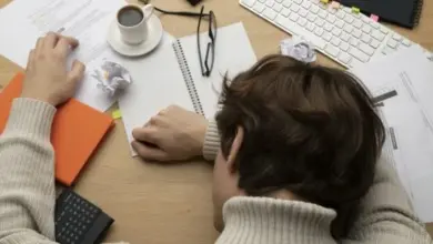 Osoba pracující u stolu s papíry, kávou a kancelářskými předměty.