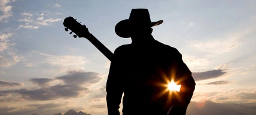 Silueta country hudebníka s kytarou před západem slunce.