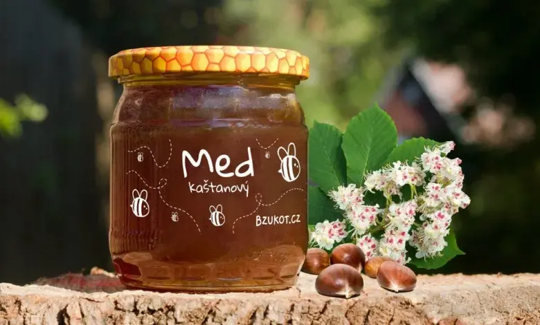 Sklenice medu z vlašského ořechu s květy a oříšky na kmeni stromu.