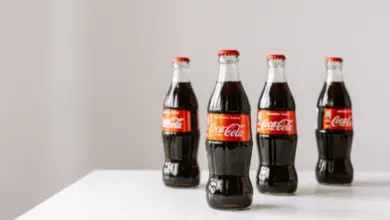 Čtyři skleněné lahve Coca-Coly na bílém povrchu.