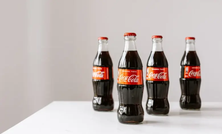 Čtyři skleněné lahve Coca-Coly na bílém povrchu.