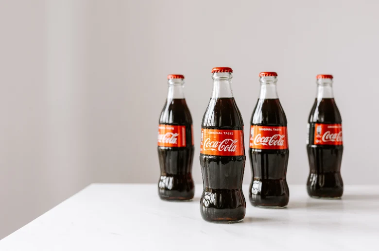 Čtyři skleněné lahve Coca-Coly na bílém povrchu.