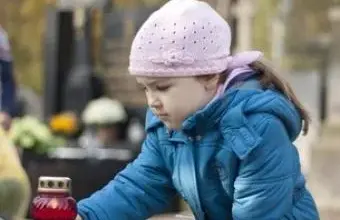 Malá dívka zapaluje svíčku na hřbitově při smuteční obřadu.