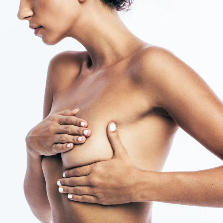 Žena s malými prsy dotýká svých hrudníku na bílém pozadí.
