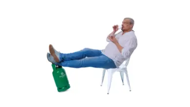Muž sedí na židli s nohama na zeleném propanovém válci.