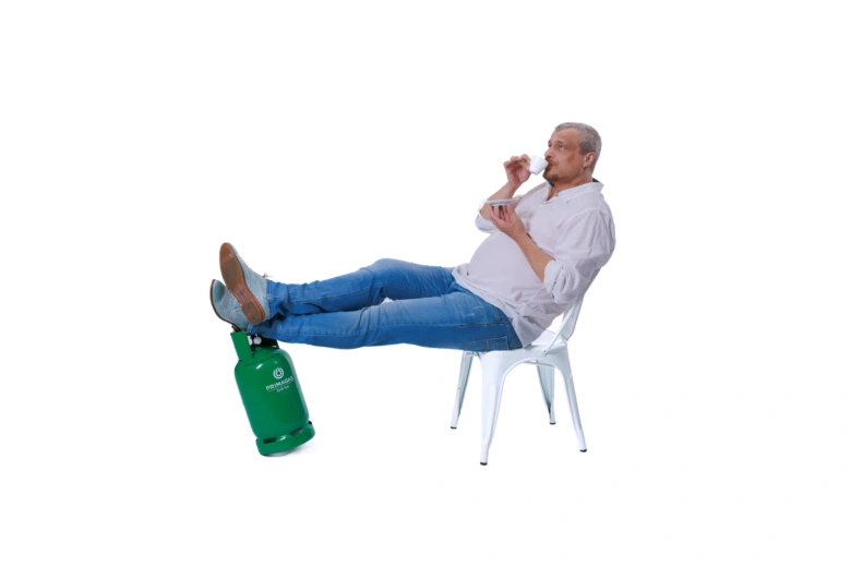 Muž sedí na židli s nohama na zeleném propanovém válci.