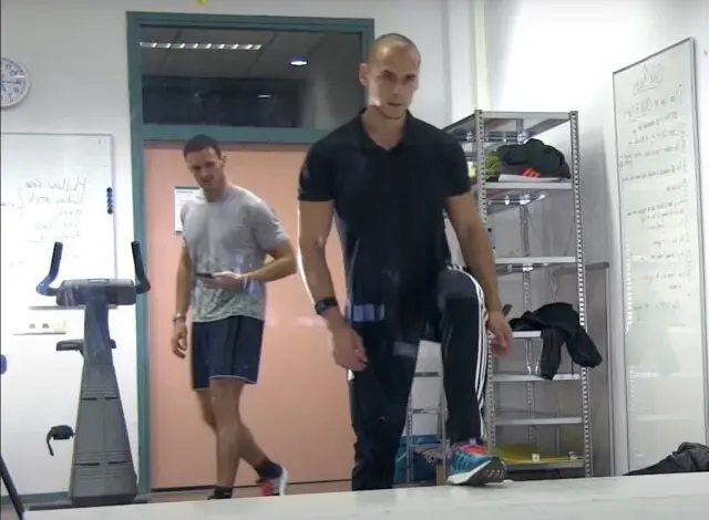 Muži se protahují v posilovně před běžeckým strojem.