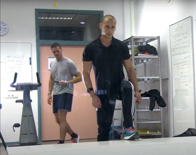 Muži se protahují v posilovně před běžeckým strojem.