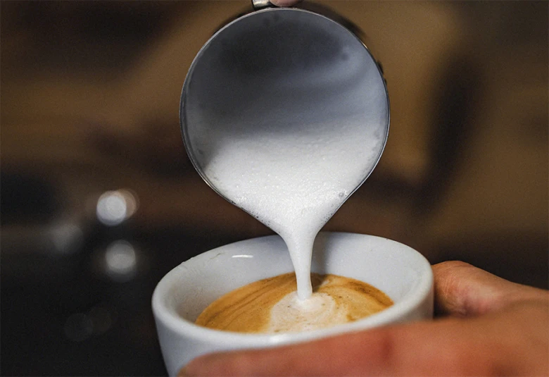 Barista nalévá mléko do kávy pro cappuccino s pěnou.