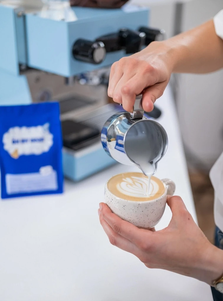 Barista nalévá mléko do kávy pro vytvoření latte artu.