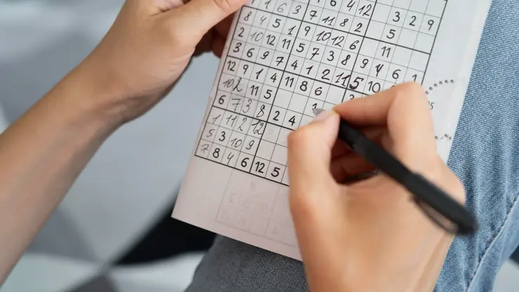 Ruce řešící sudoku s tužkou na papírové mřížce