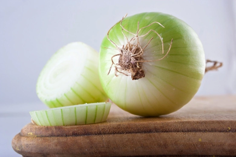 Celá cibule nakrájená na polovinu s řezem na dřevěném prknu.