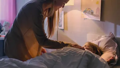 Matka ukládá spát své dítě do postele v noci.
