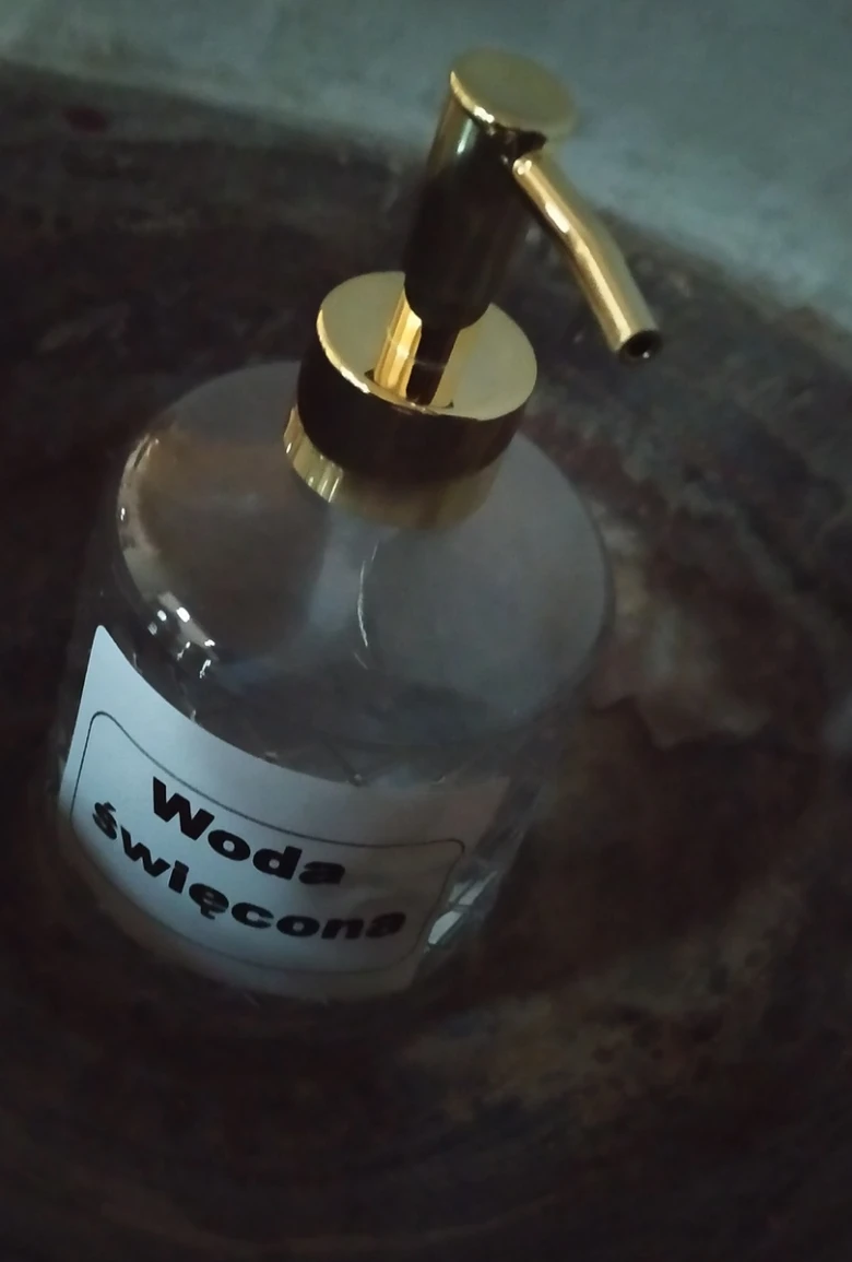 Skleněná lahvička s čerpacím mechanismem označená jako svatá voda.