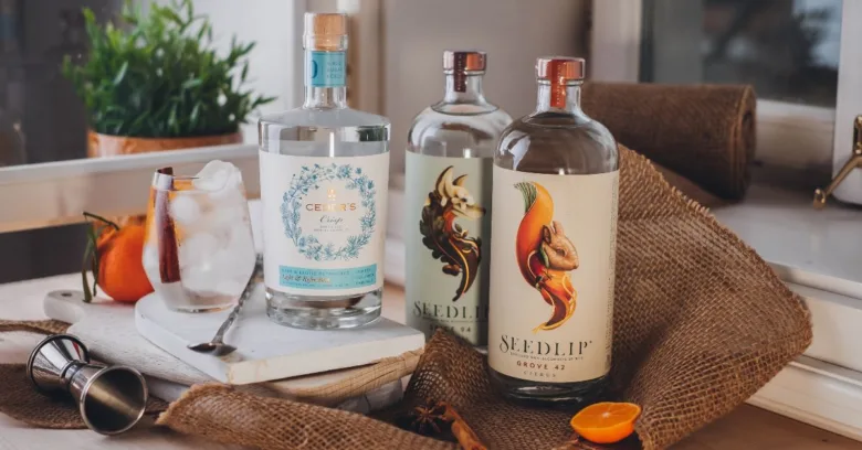 Tři lahve nealkoholických nápojů značky Seedlip na stole s ozdobami.