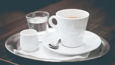 Bílá šálka s kávou a sklenička vody na stříbrném podnose.