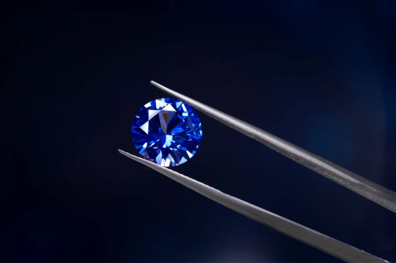 Modrý diamant držený klemou na tmavém pozadí.