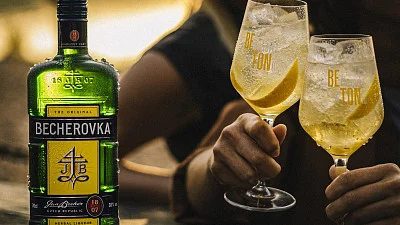 Fotka lahve Becherovky s citronem a ledem ve sklenicích.