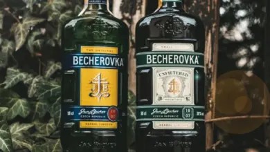 Dvě lahve Becherovky před zelenou stěnou s liánami.