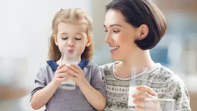 Matka s dcerou pijí mléko z sklenic v kuchyni.