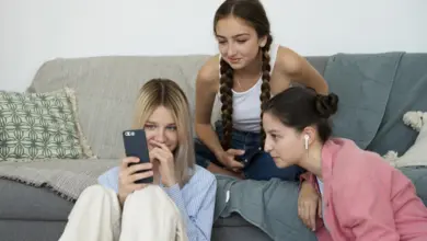 Tři dívky sedí na gauči s mobilními telefony.
