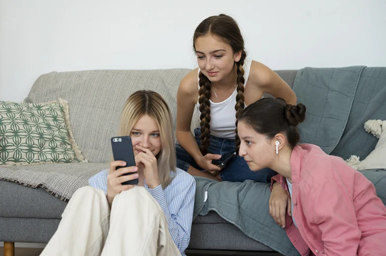 Tři dívky sedí na gauči s mobilními telefony.