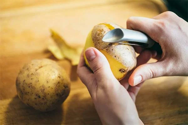 Ruce škrábou kůru z brambory pomocí ošklivače.