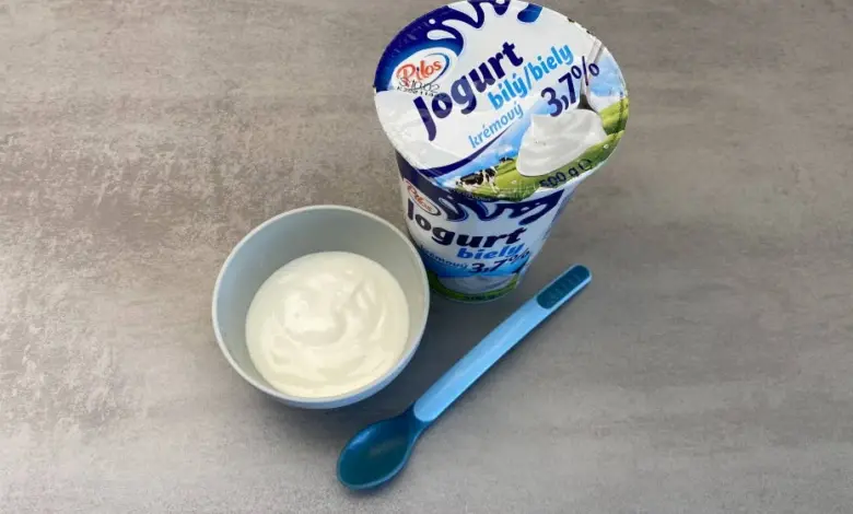 Bílý jogurt v misce s modlou lžičkou pro děti.