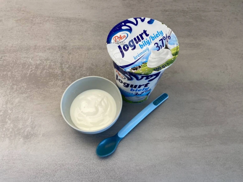 Bílý jogurt v misce s modlou lžičkou pro děti.