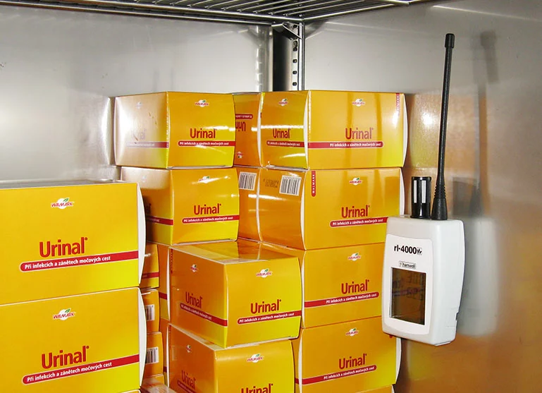 Digitální teploměr s vlhkoměrem v lékárně vedle balení léků.