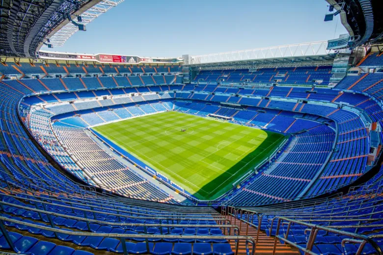Prázdné fotbalové hřiště v areálu stadionu s modrými sedadly.