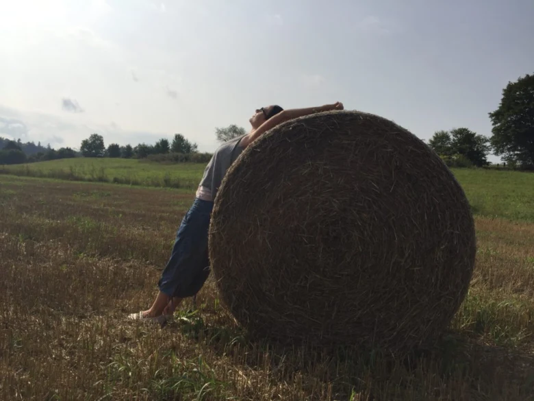 Osoba se opírá o slámovou balu na louce.