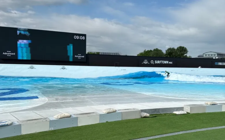 Umělá vlna ve sportovním bazénu s surferem na akci.