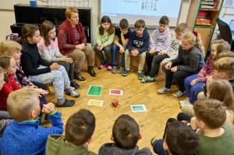 Děti sedí v kruhu ve třídě s učitelem při společné činnosti.