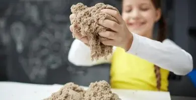 Dívka drží hrst kinetického písku nad bílou plochou.