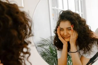 Dívka se dívá do zrcadla s výrazem smutku.