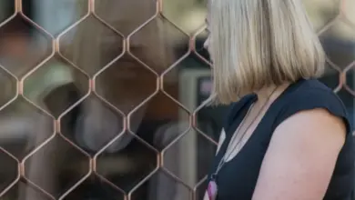Žena sedí u plotu s mříží a pohlédá do dálky.