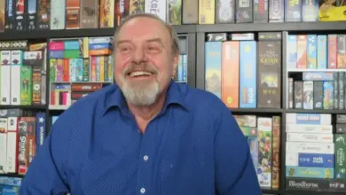 Usmívající se muž před regály s deskovými hrami.
