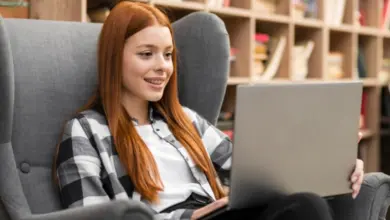 Mladá žena s červenými vlasy sedí v křesle a pracuje na notebooku.