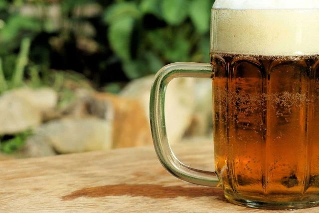 Pivo v skleněném poháru na dřevěné desce venku.