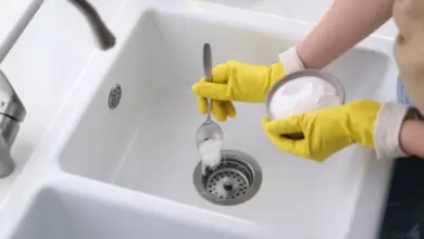 Člověk v žlutých rukavicích nalévá jedlou sodu do odtoku.