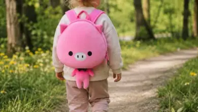Dívka s růžovým batohem v tvare prasátka chodí lesní cestou.