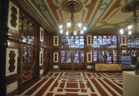 Vstupní hala v art nouveau stylu s dlažbou a dřevěnou výzdobou.
