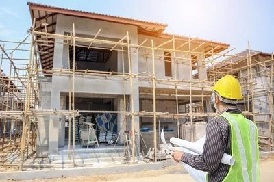 Architekt s plány na staveništi před nedokončenou budovou.