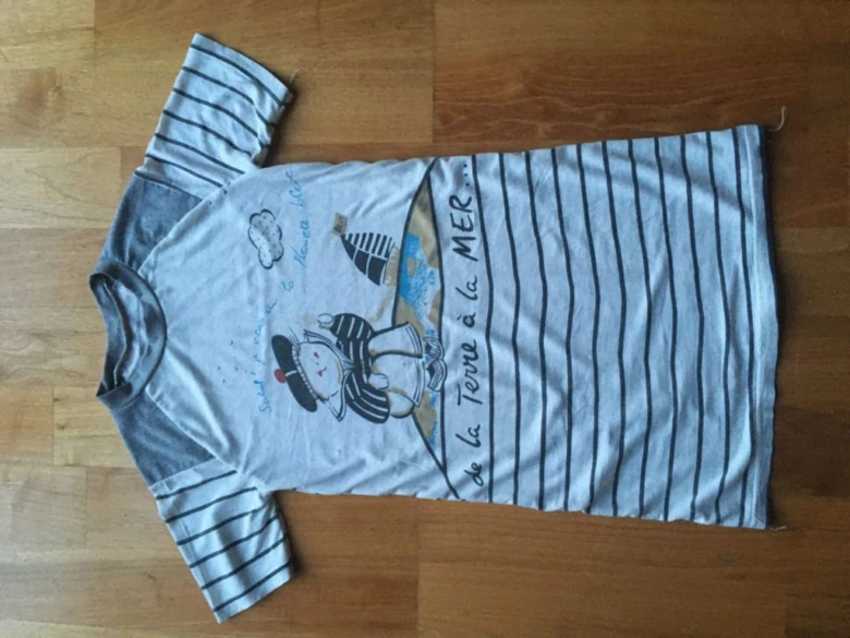 Bílá trička s proužky a šedými raglánovými rukávemi na dřevěném podlaze.