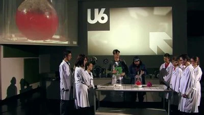 Skupina lidí v laboratorních pláštích s chemickým vybavením.