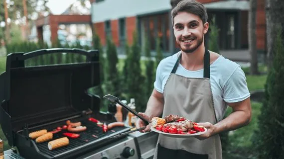 Muž griluje maso s bramborami venku v létě.